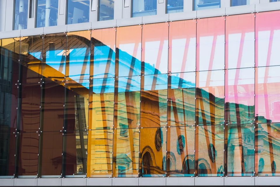 Front of a building with tall glass walls reflecting another nearby structure